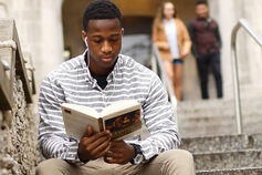 A Black student reads on the steps of a campus building.